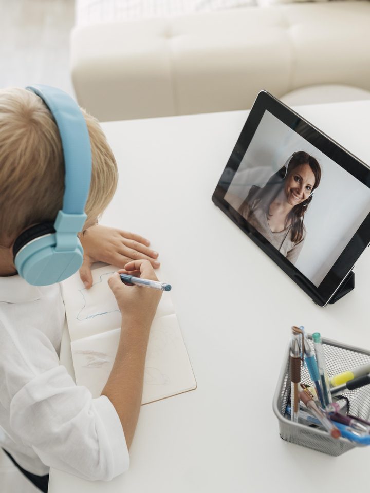 A boy in headphones taking notes during a live online Kidgency lesson with his tutor