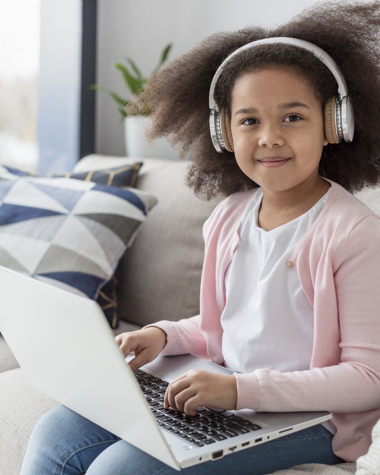 A girl in headphones taking a live online Kidgency lesson on her laptop at home